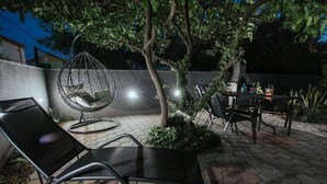An outdoor patio with hexagonal tiles, a hanging chair, a table with chairs, and a small garden area. - Apartment Florio (Trogir)