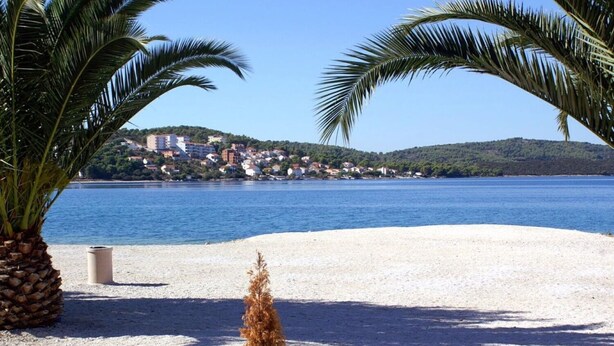 A beach with white sand, a clear blue sea, and a hill with buildings in the background. - Apartment Florio (Trogir)