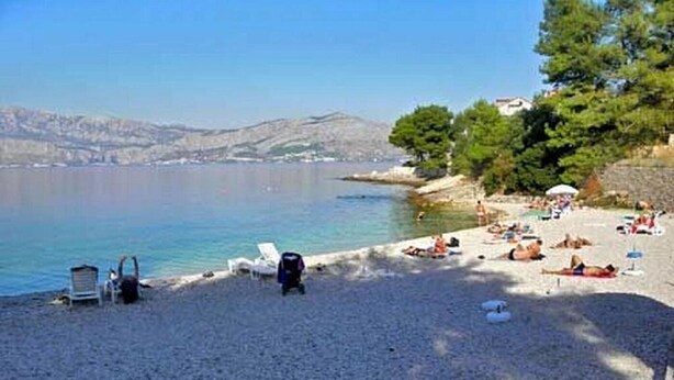 Une plage de galets avec des transats et des parasols, un ciel dégagé et des collines lointaines.