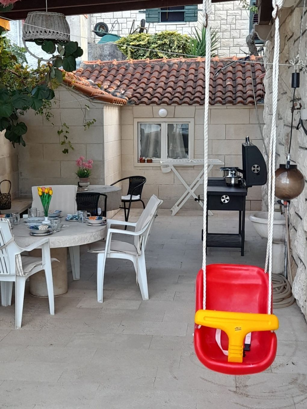 An outdoor patio with a round table and chairs, a hanging swing, and a barbecue grill.