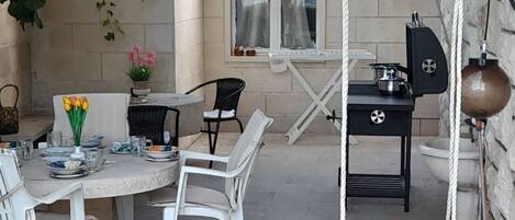 An outdoor patio with a round table and chairs, a hanging swing, and a barbecue grill.