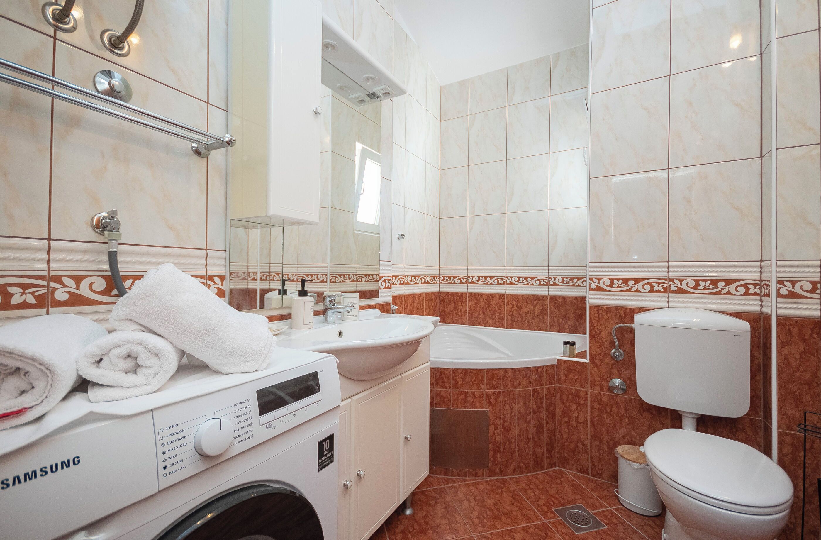 Egy modern fürdőszoba mosógéppel, mosdókagylóval és WC-vel felszerelve.