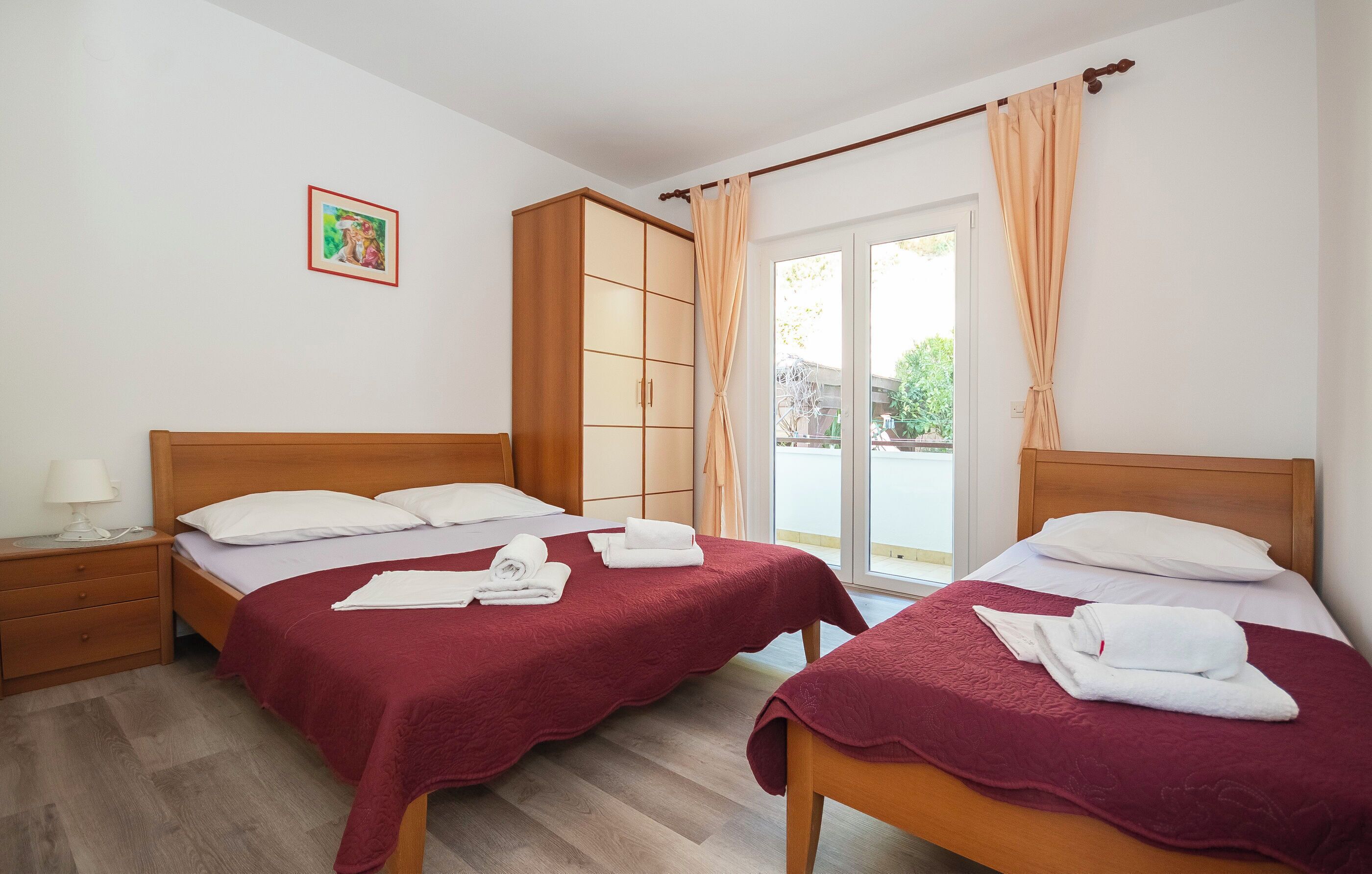 Habitación de hotel con dos camas, cabeceros de madera, un armario y un ventanal con cortinas.