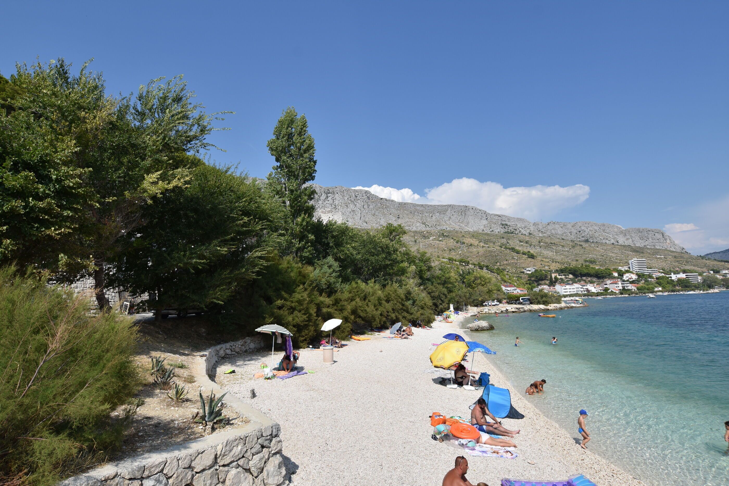 A beach with clear water, people sunbathing, and a mountain in the background.