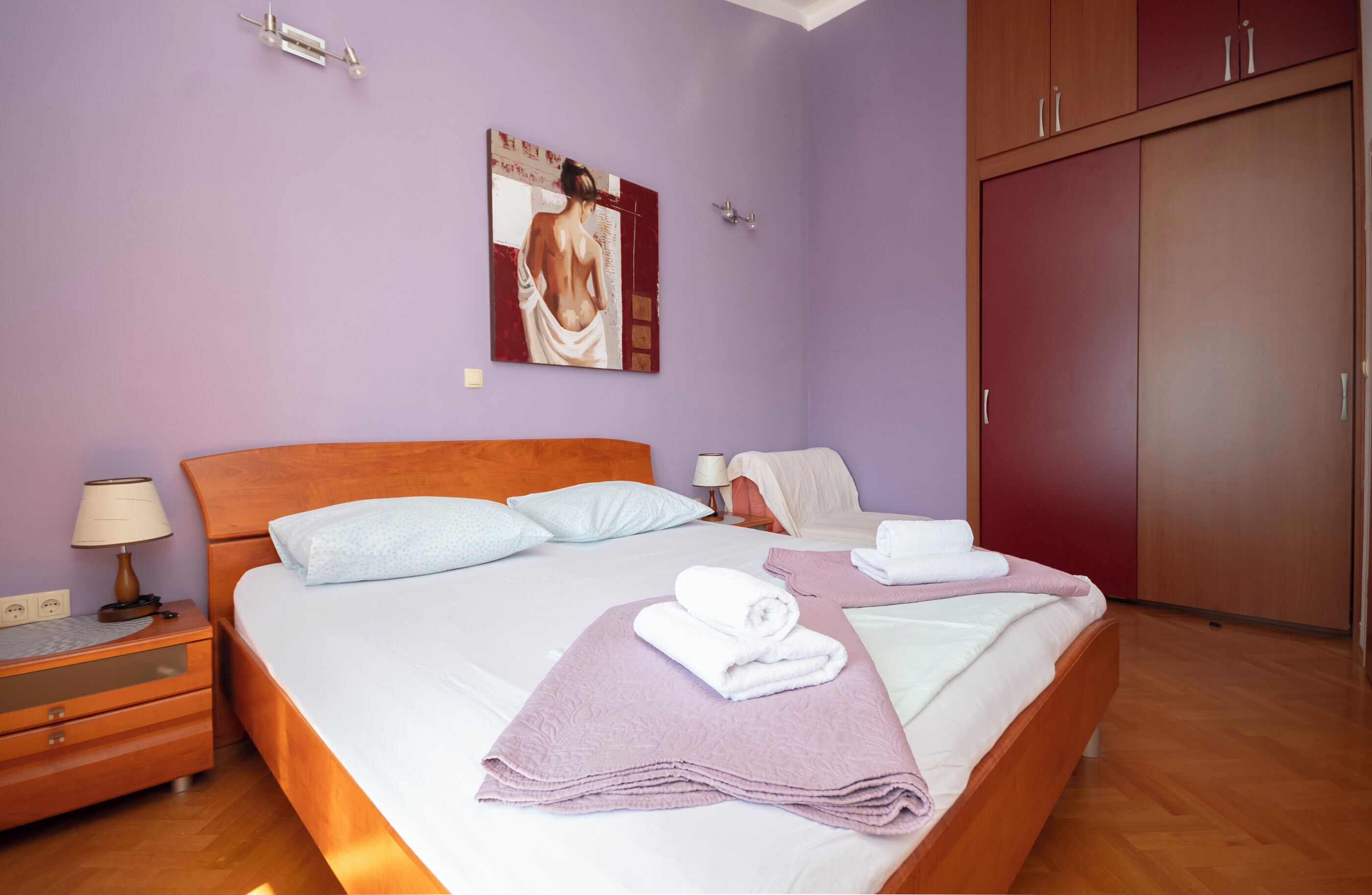 A bedroom with a bed, nightstands, a wardrobe, and a painting on the wall.