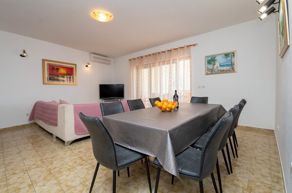 A dining area with a table set for six, a sofa with a pink blanket, and a TV on the wall. - Apartment Karlo (Dugi Rat)