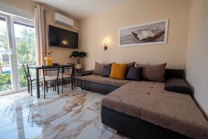 A modern living room with a sectional sofa, a dining table with chairs, and a large window with curtains. - Apartments Relax Suites (Novi Vinodolski)