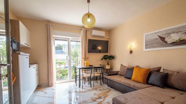 A modern living area with a sofa, a dining table, and a TV mounted on the wall. - Apartments Relax Suites (Novi Vinodolski)