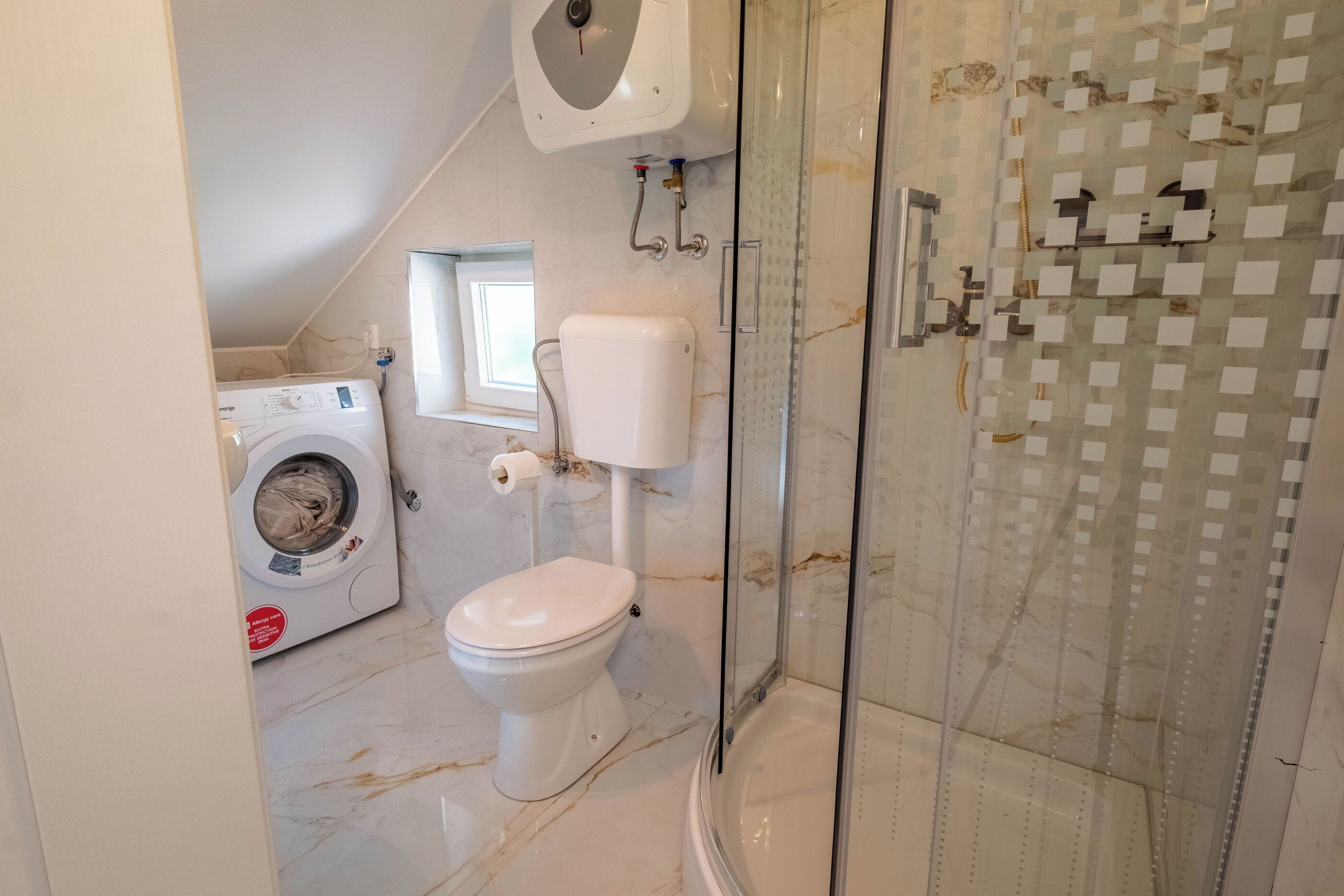 Ein Badezimmer mit Waschmaschine, Toilette und Duschkabine.