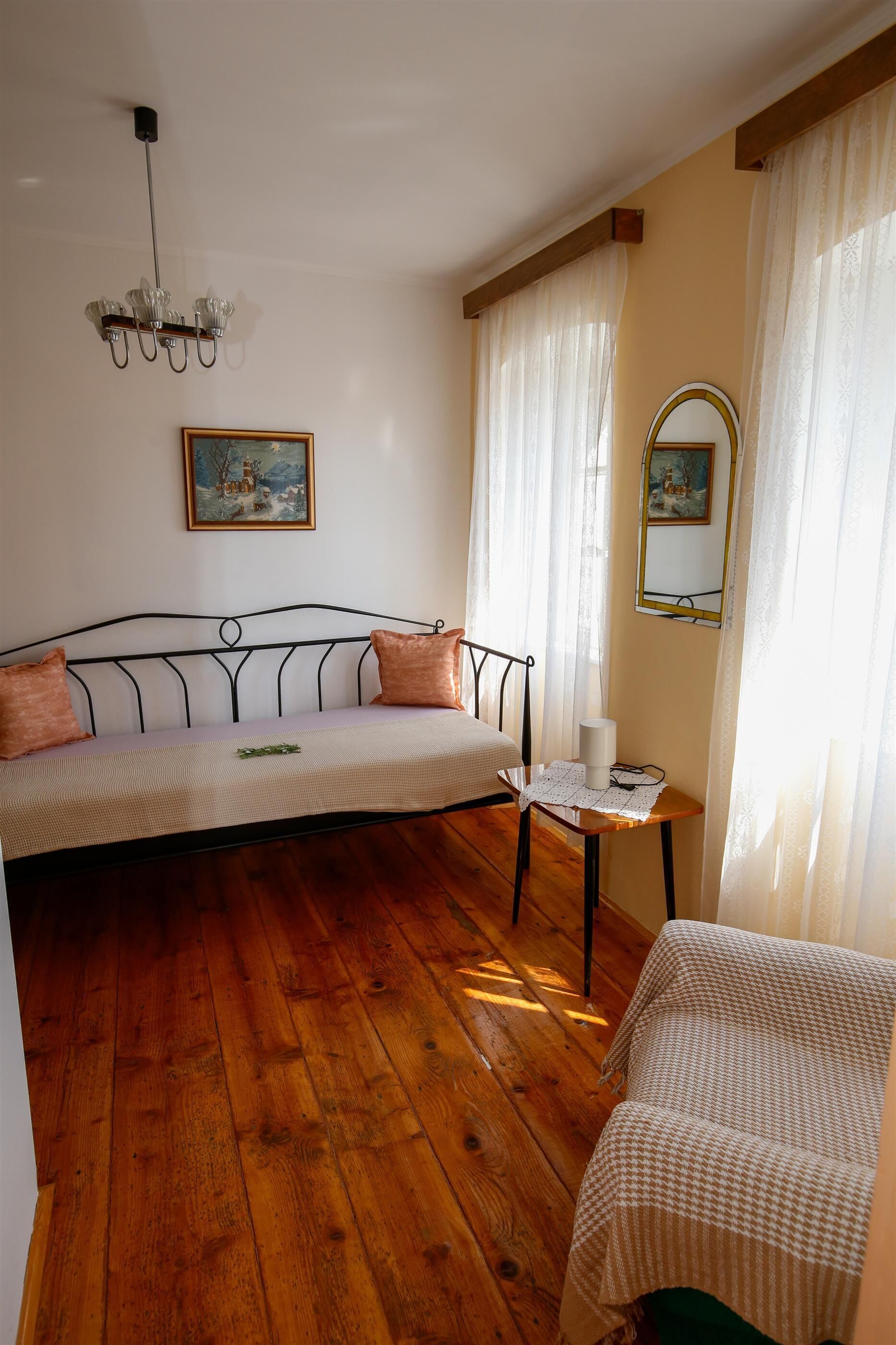 Une pièce avec un plancher en bois, un canapé avec des coussins, une petite table avec une lampe et un tableau accroché au mur.