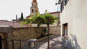 A courtyard with a stone wall, a metal gate, and a building with a tiled roof and a bell tower. - House Dragica (Vinodol)