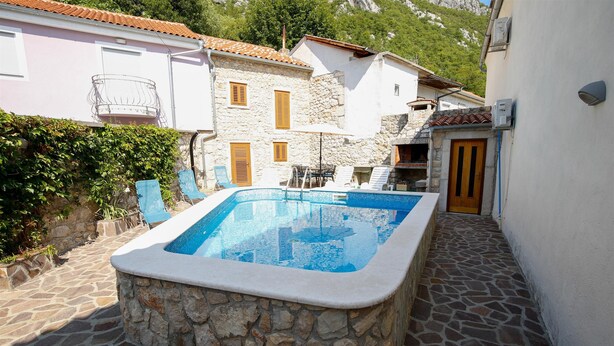 A stone pool with a tiled deck, surrounded by stone walls and a wooden door. - House Dragica (Vinodol)