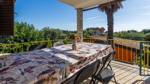 A covered outdoor dining area with a table set for two, surrounded by chairs, and a potted plant on the table. - Apartment Lili (Umag)