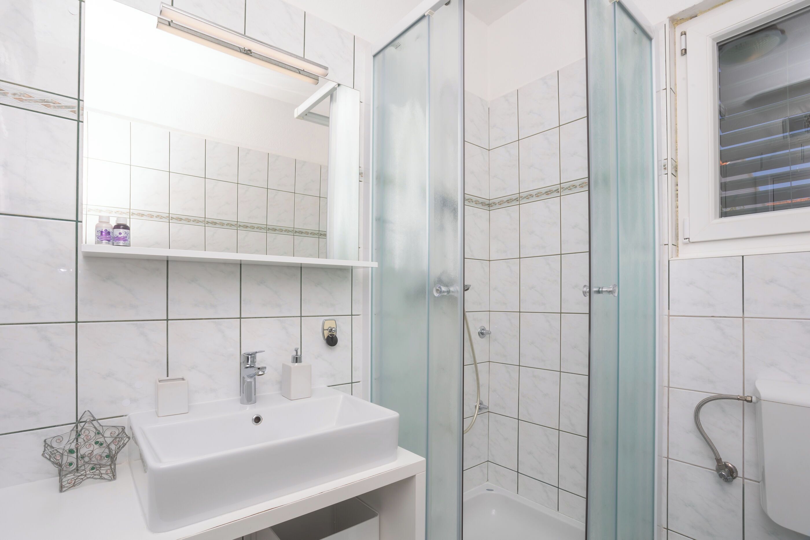Ein Badezimmer mit einem weißen Waschbecken, einer Duschkabine aus Glas und einer Toilette.