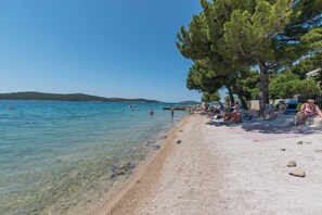 A beach with clear water, people sunbathing, and a tree-lined area. - Apartments Lavandela Girandela (Sibenik)