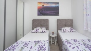 Une chambre avec deux lits, chacun agrémenté de linge de lit aux motifs de lavande, une petite table blanche et un tableau représentant un champ de lavande accroché au mur.