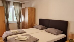 A double bed with two pillows, a wooden wardrobe, and a window with curtains. - House Dalmatika Zaton (Nin)