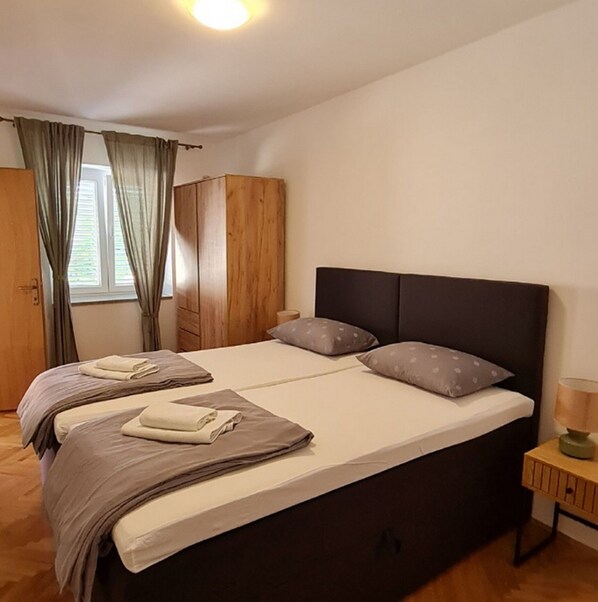 A double bed with two pillows, a wooden wardrobe, and a window with curtains. - House Dalmatika Zaton (Nin)