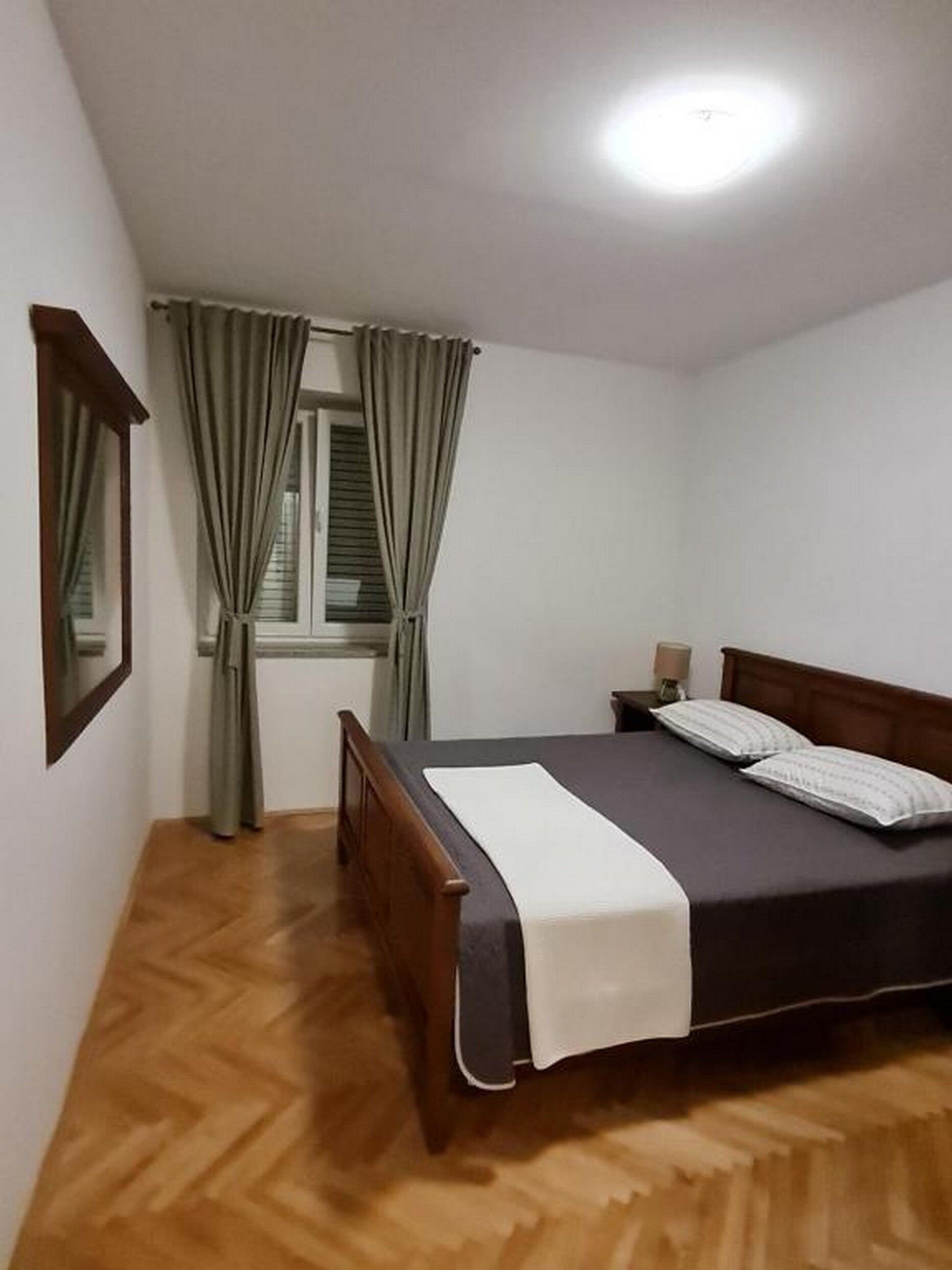 A bedroom with a wooden bed, a window with curtains, a nightstand, and a mirror.
