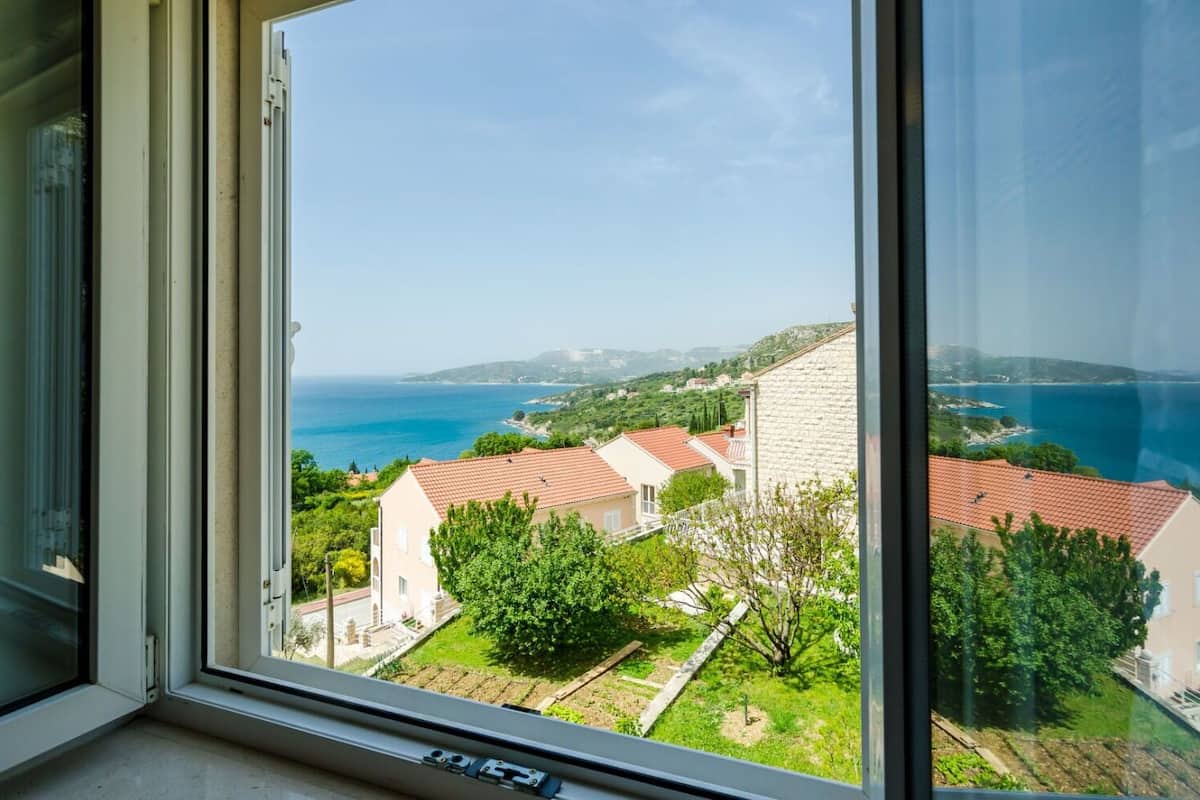 A view from a window overlooking a coastal area with buildings and a clear blue sea.