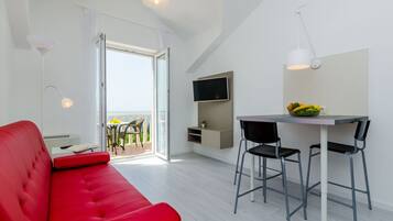 Una sala de estar moderna con un sofá rojo, una mesa de comedor con dos sillas, un televisor montado en la pared y un balcón con vistas.