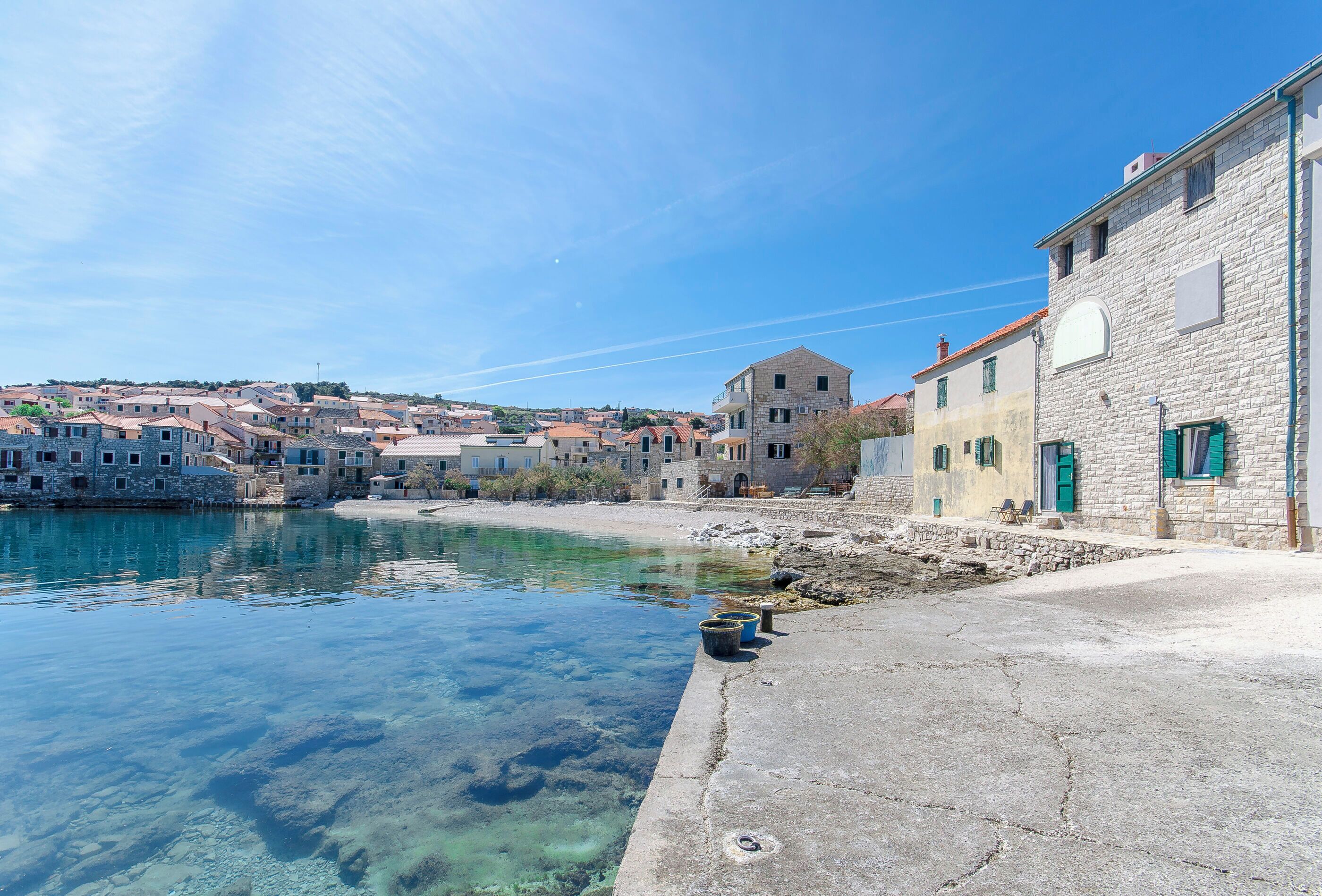 A coastal town with stone buildings, clear water, and a paved walkway along the shore.