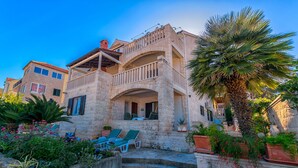 A stone building with a balcony, outdoor seating, and a palm tree. - Apartments Paco (Postira)