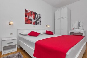 A bedroom with a bed, white wardrobe, bedside table, and a wall-mounted mirror. - Apartments Smiljka (Makarska)
