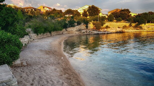 A beach with clear water, a stone wall, and houses in the background. - Apartments Mare Family Only (Kolan)