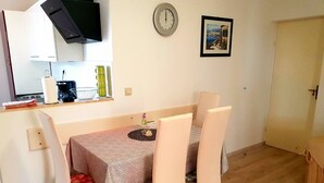 A small dining area with a table and chairs, a clock on the wall, and a door to the right. - Apartments Mare Family Only (Kolan)