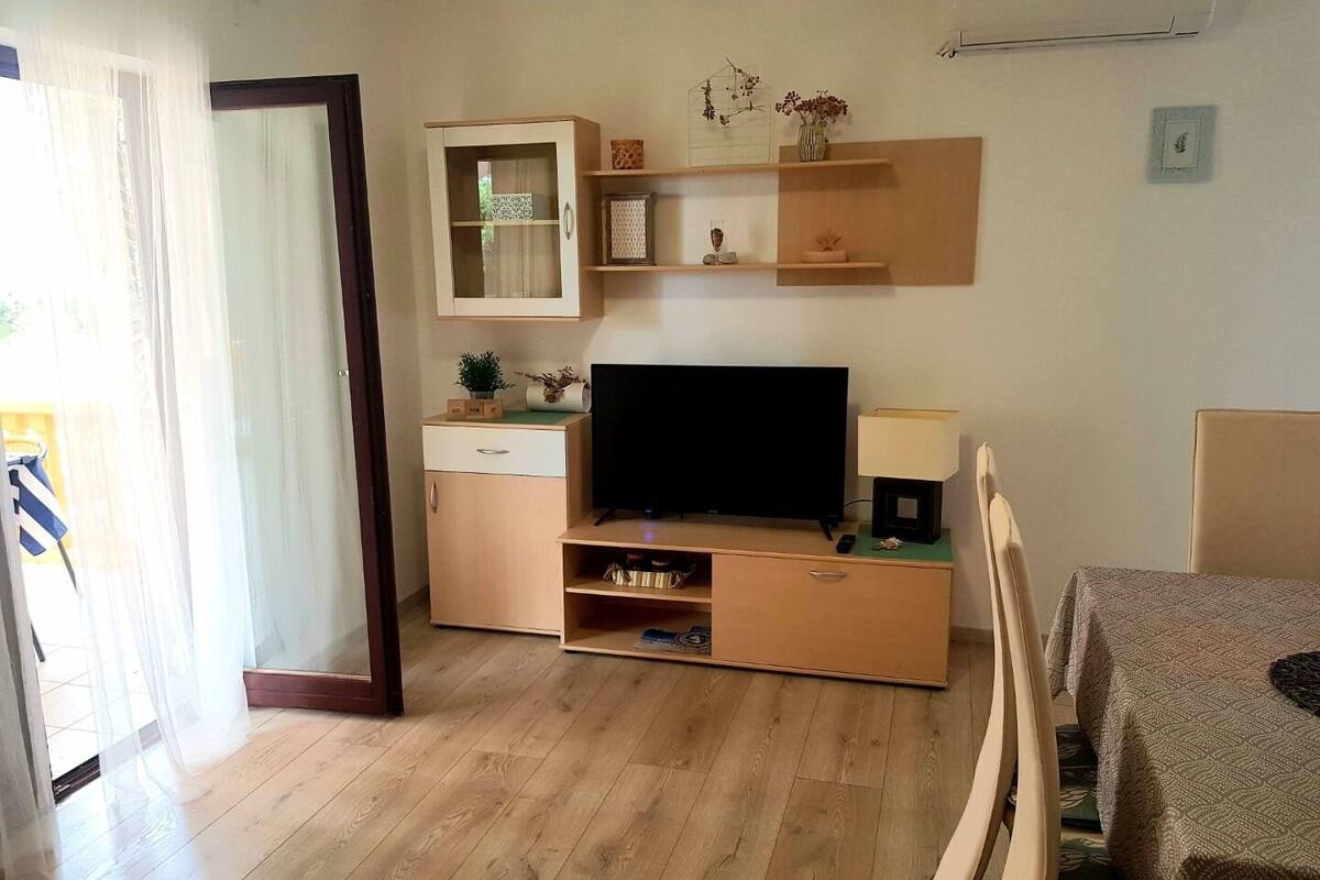 A modern living room with a flat-screen TV, wooden furniture, and a sliding glass door leading to a balcony.