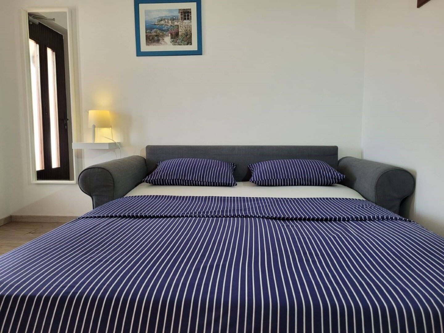 A bedroom with a bed, pillows, a nightstand, a lamp, and a framed picture on the wall.