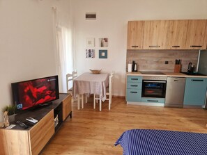 A compact living space with a television, a dining table, a kitchenette, and a bed. - Apartments Mare Family Only (Kolan)
