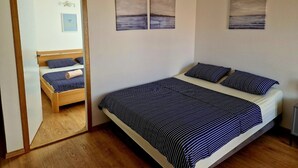 A bedroom with a large bed, a wooden wardrobe, and a mirror reflecting the room. There are three paintings on the wall. - Apartments Mare Family Only (Kolan)
