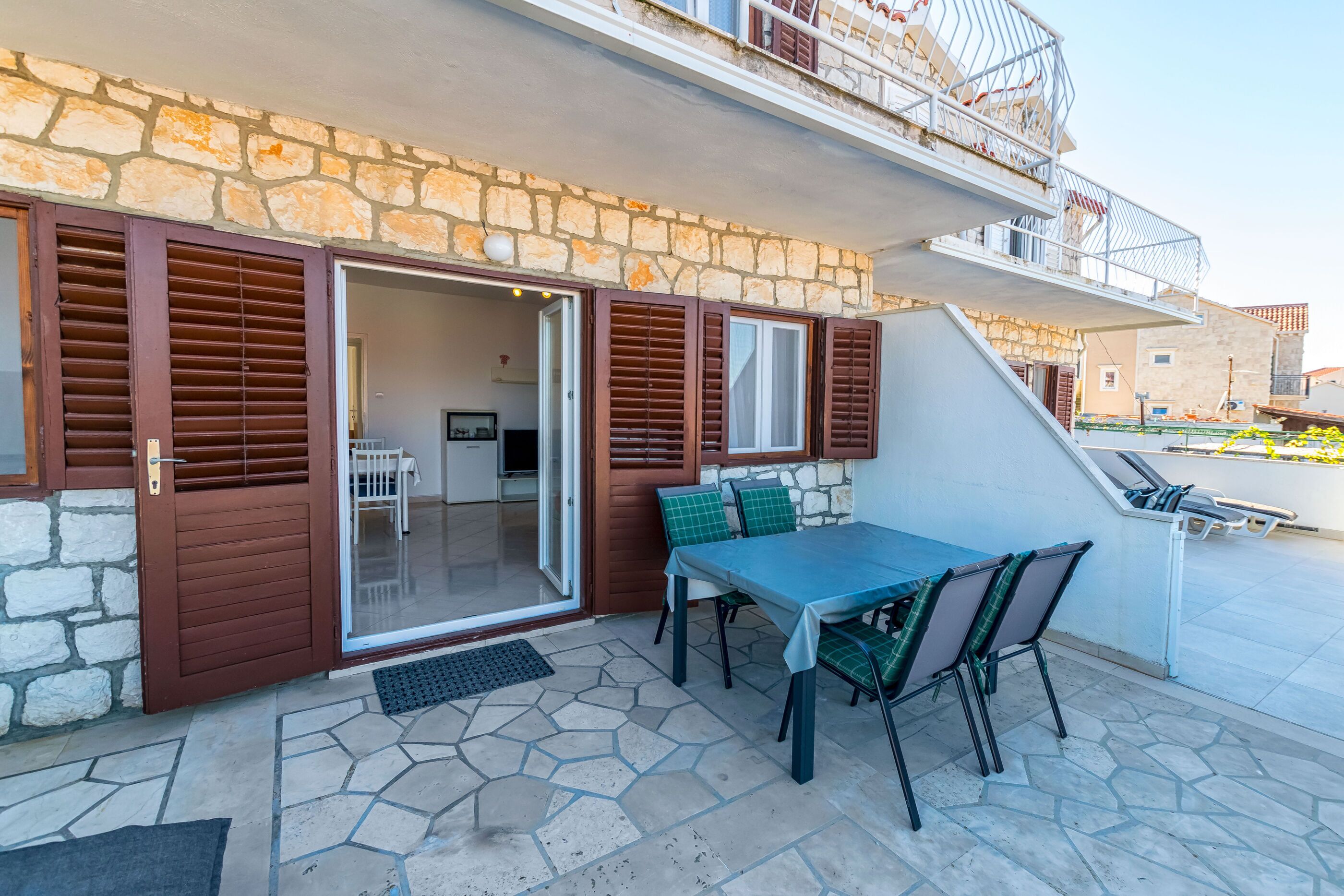 A patio with a table and chairs, a stone wall, and a balcony with railings.