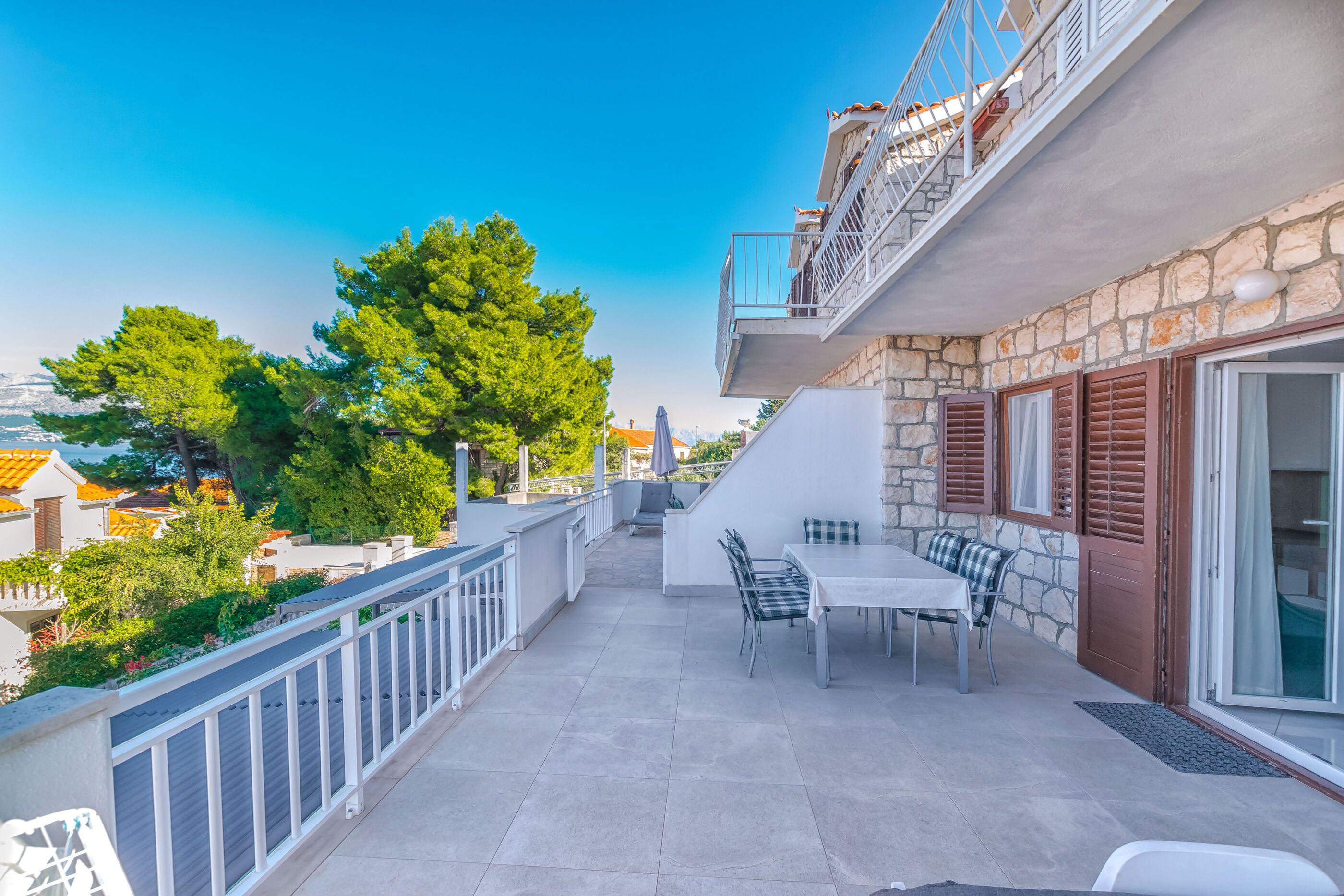 Un balcón con mesa y sillas, con vista a una zona residencial con árboles y edificios.