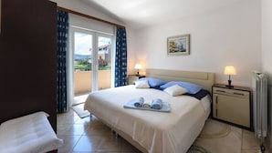 A hotel room with a large bed, two bedside tables with lamps, a view of the outdoors through a sliding door, and a painting on the wall. - Apartments Ivo (Kastela)