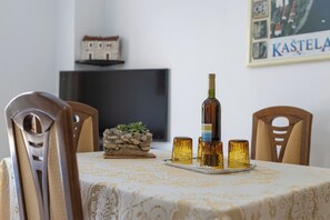 A dining table with a bottle and glasses, a small plant, and a framed picture on the wall. - Apartments Ivo (Kastela)