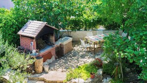 A patio area with a brick barbecue, outdoor seating, and lush greenery. - Apartments Ivo (Kastela)