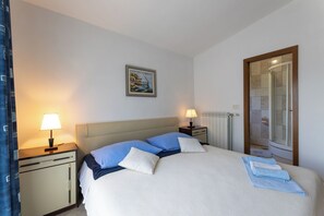 A neatly made bed with blue and white bedding, a bedside table with a lamp, and a framed picture on the wall. - Apartments Ivo (Kastela)