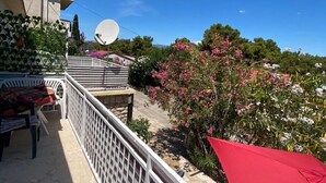 Een balkon met een witte leuning, een rode parasol en een schotelantenne.