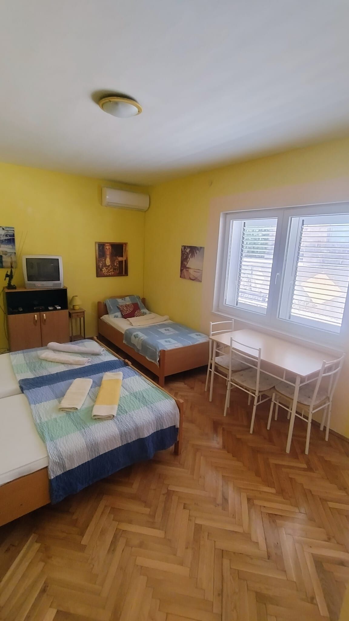 A room with two beds, a desk, a chair, a television, and artwork on the walls.