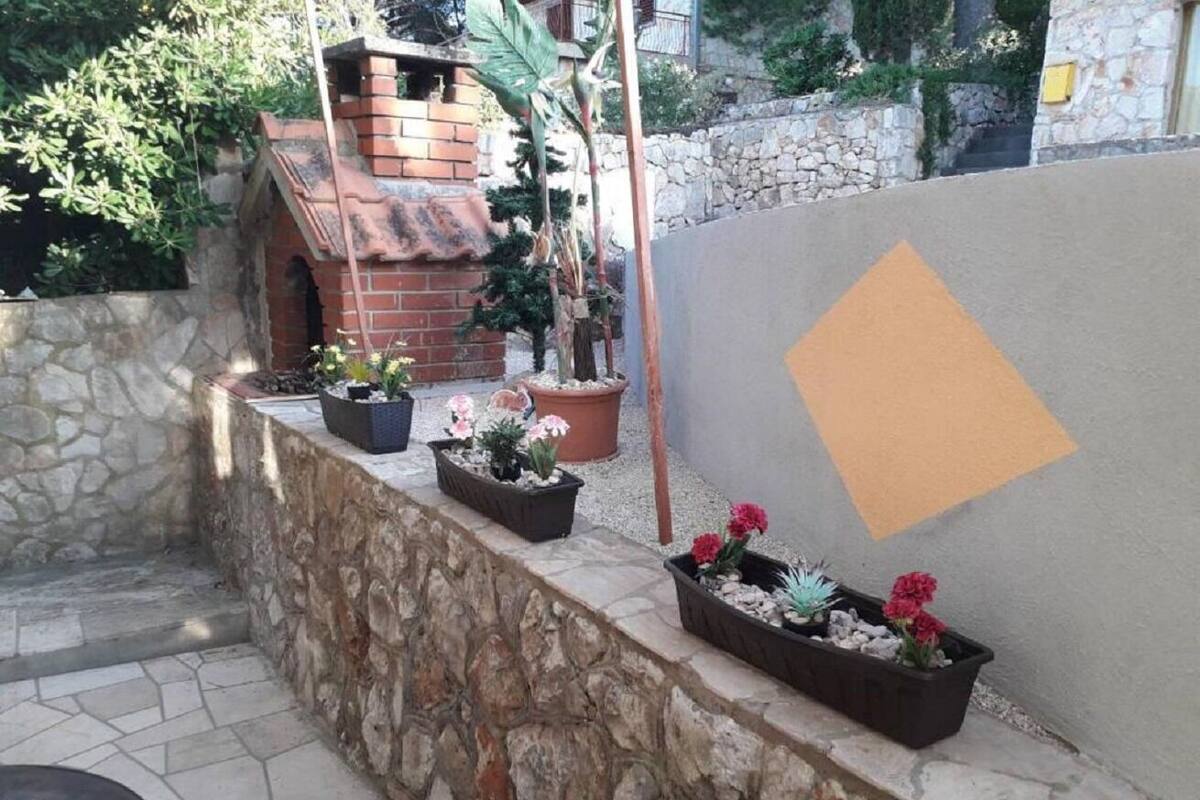 A stone wall with potted plants and a brick structure in the background.