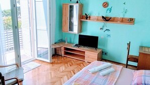 Een slaapkamer met een bed, een bureau, een televisie en een schuifdeur naar een balkon.