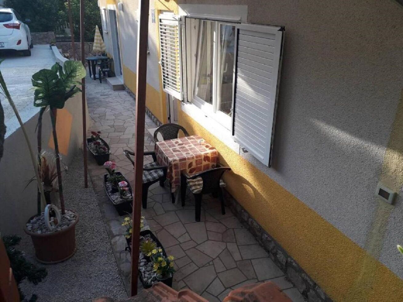 A patio area with a table and chairs, potted plants, and a window with blinds.