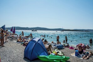 A beach with people sunbathing, swimming, and a tent set up. - Apartment Grdelin (Biograd na Moru)