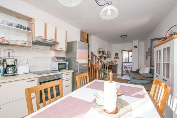 A modern kitchen with white cabinets, a stainless steel refrigerator, and a dining area with a table set for two. - Apartment Grdelin (Biograd na Moru)