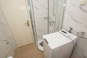 A bathroom with a glass shower enclosure, a white washing machine, and a toilet. - Apartment Grdelin (Biograd na Moru)