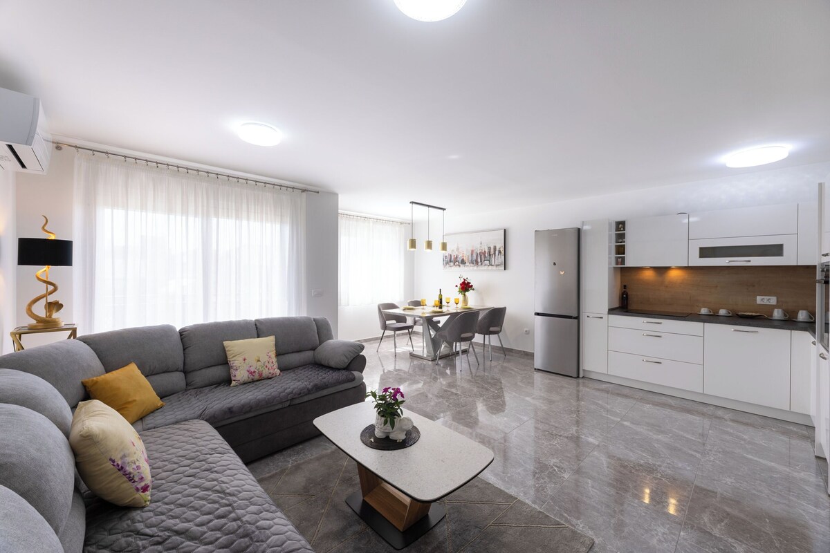 Una sala de estar moderna con un sofá gris, una mesa de centro y un comedor con una mesa y sillas blancas.