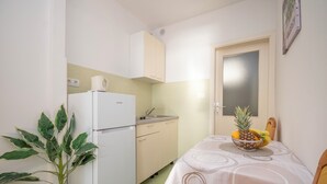 A compact kitchen with a refrigerator, sink, and a dining table with a fruit bowl. - Apartment Ivana (Omis)